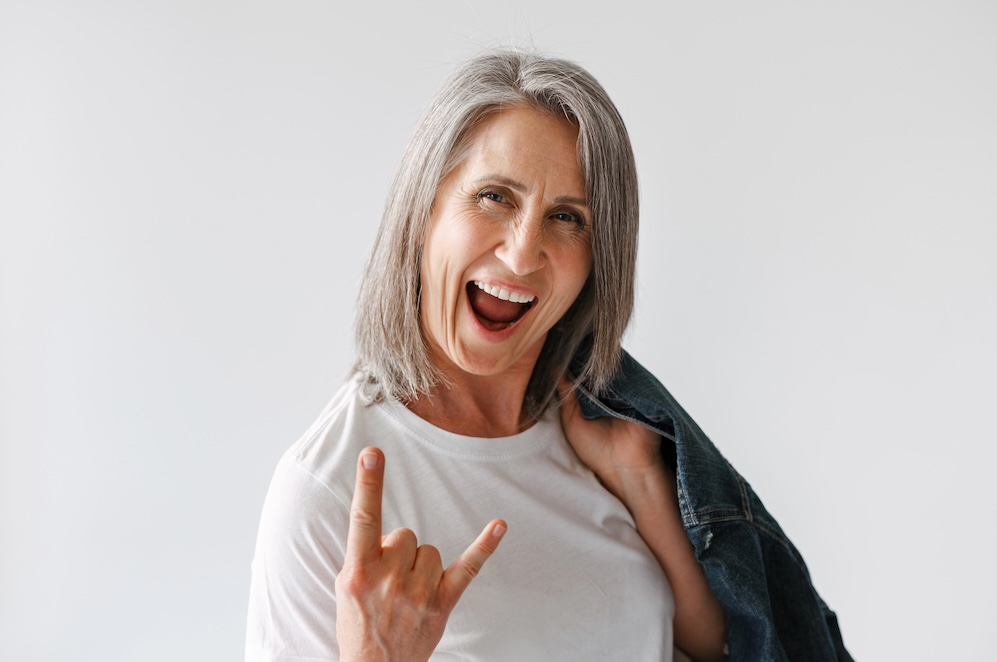 Grey senior woman gesturing while posing with denim jacket isolated over white background